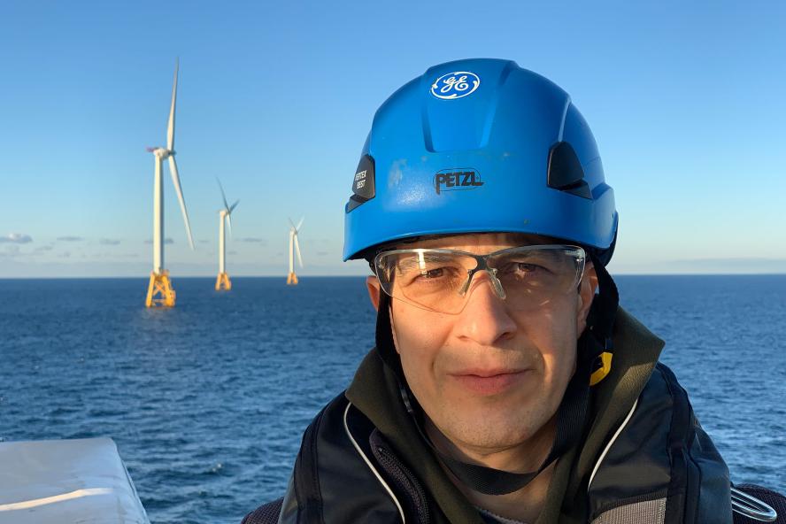 Tufts Professor Babak Moaveni with hard hat and the Block Island Wind Farm in the background
