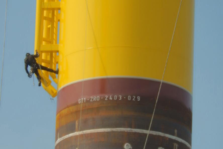Worker scaling an offshore wind foundation with ropes